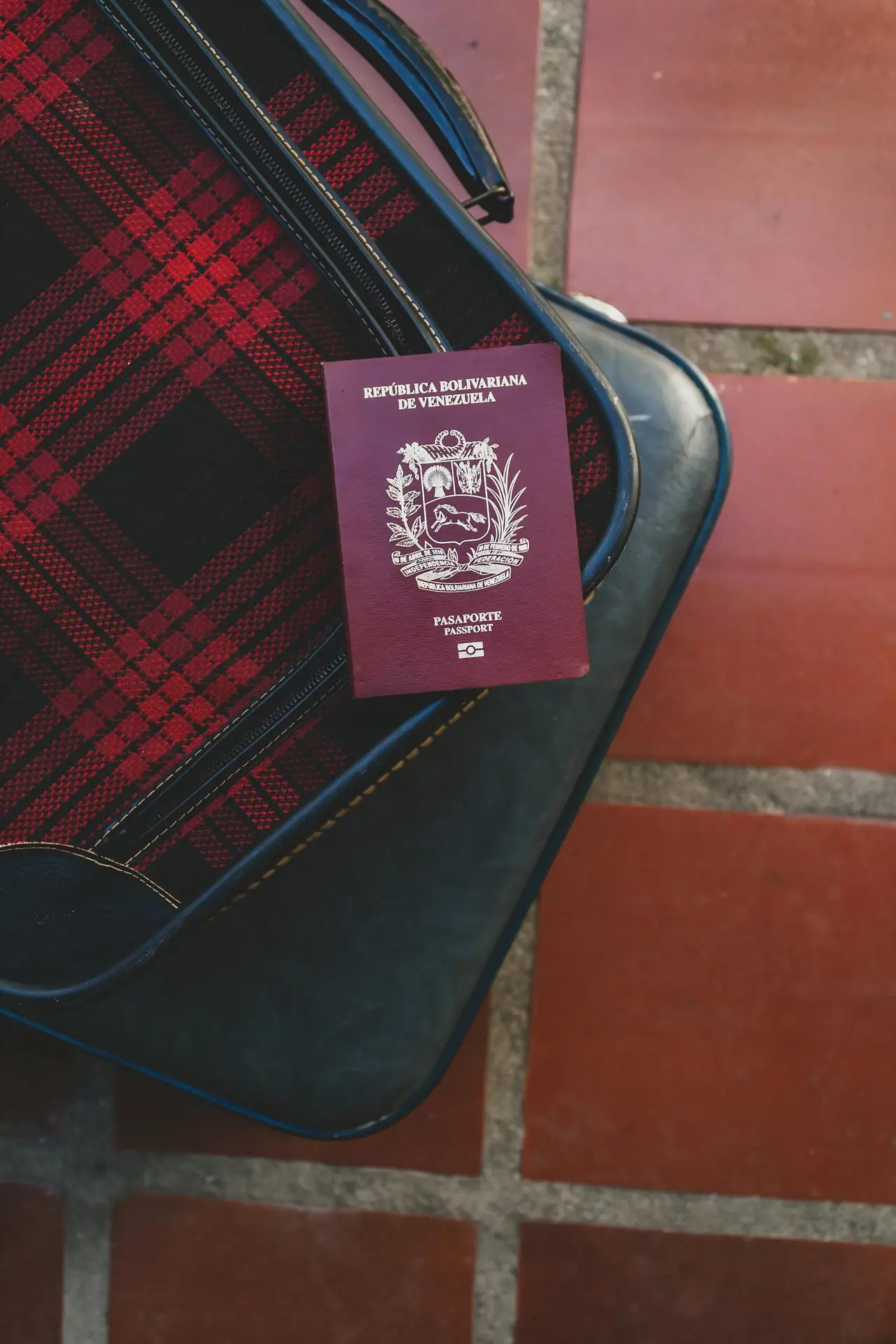 Close-up of Venezuelan passport atop plaid suitcase on tiled floor.